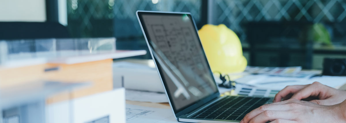 laptop on desk with papers and hard hat